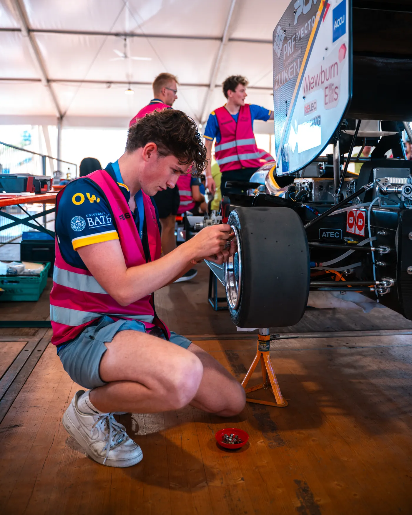 Ola Werring crouched beside the car at Formula Student Germany, fitting a wheel to the front upright
