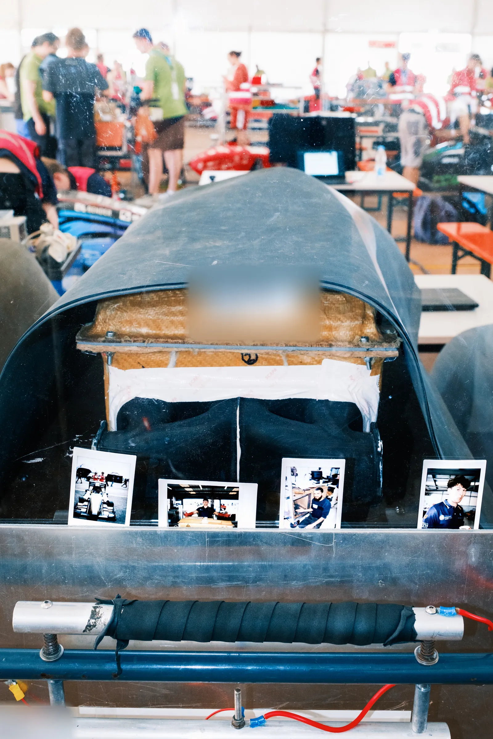 The trolley at scrutineering with the accumulator sealed under its cover on the worktop, polaroids of the team along the front edge